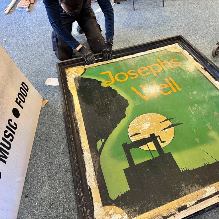Green Joseph's Well metal sign on the floor being taken out of its frame.