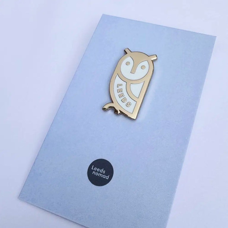 Gold and white owl badge with the word Leeds embedded in it.