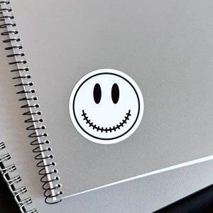 White Acid House smiley sticker on a notebook with a scary stitched mouth design.